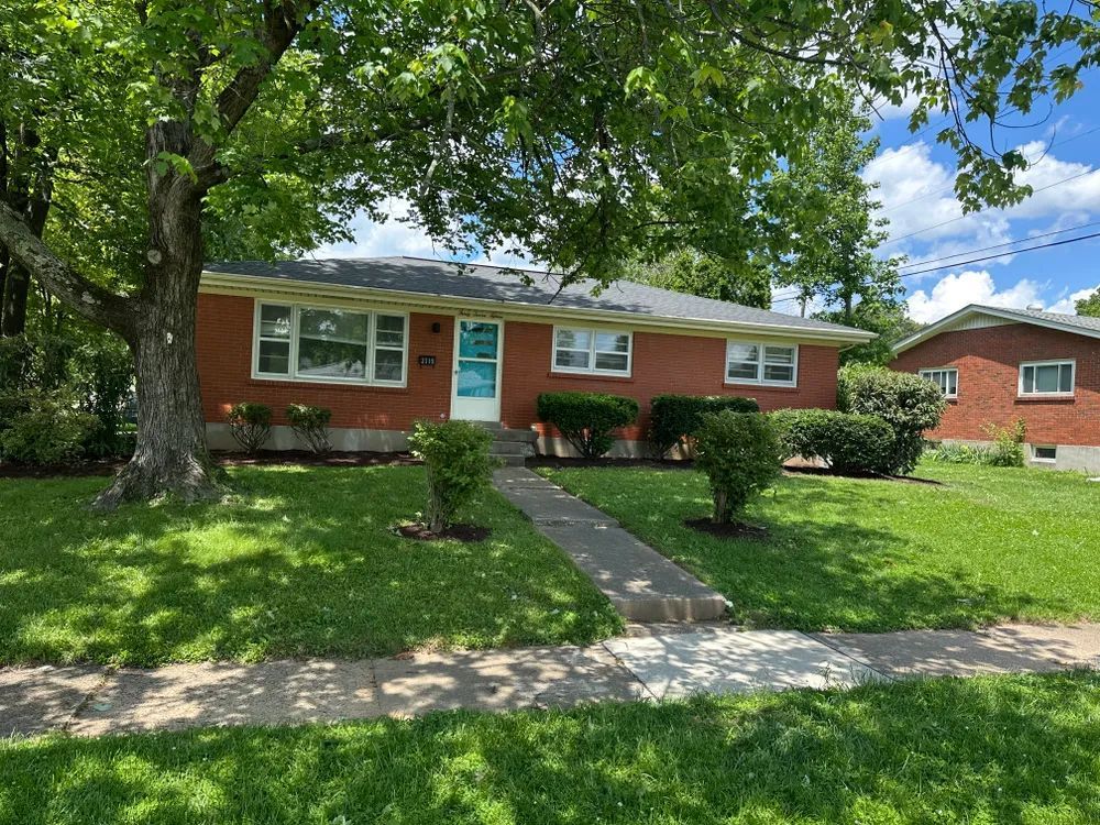 A brick house with a large lawn and a tree in front of it.