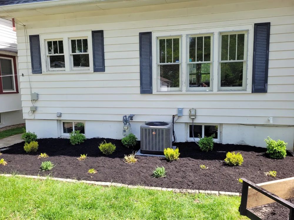 A white house with black shutters and a lawn in front of it.