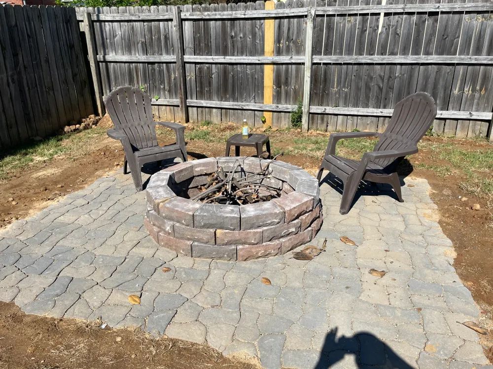 A fire pit with two chairs in front of a wooden fence.