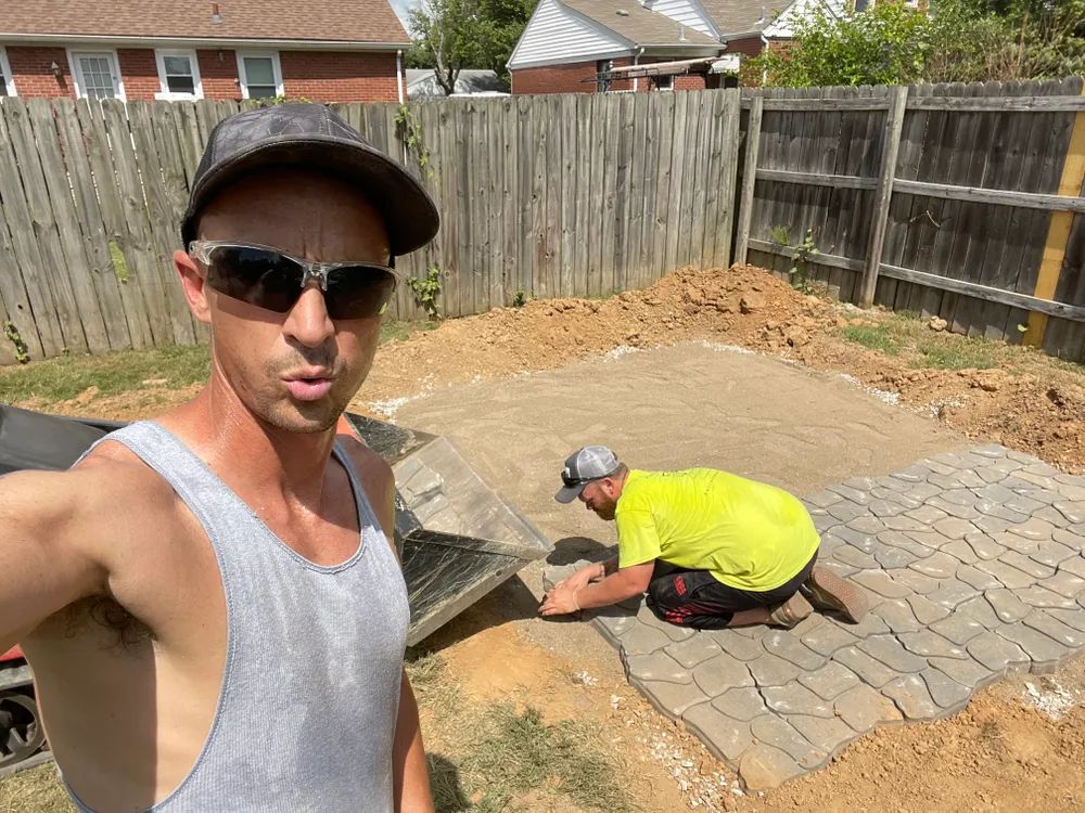 Two men are working on a patio in a backyard.
