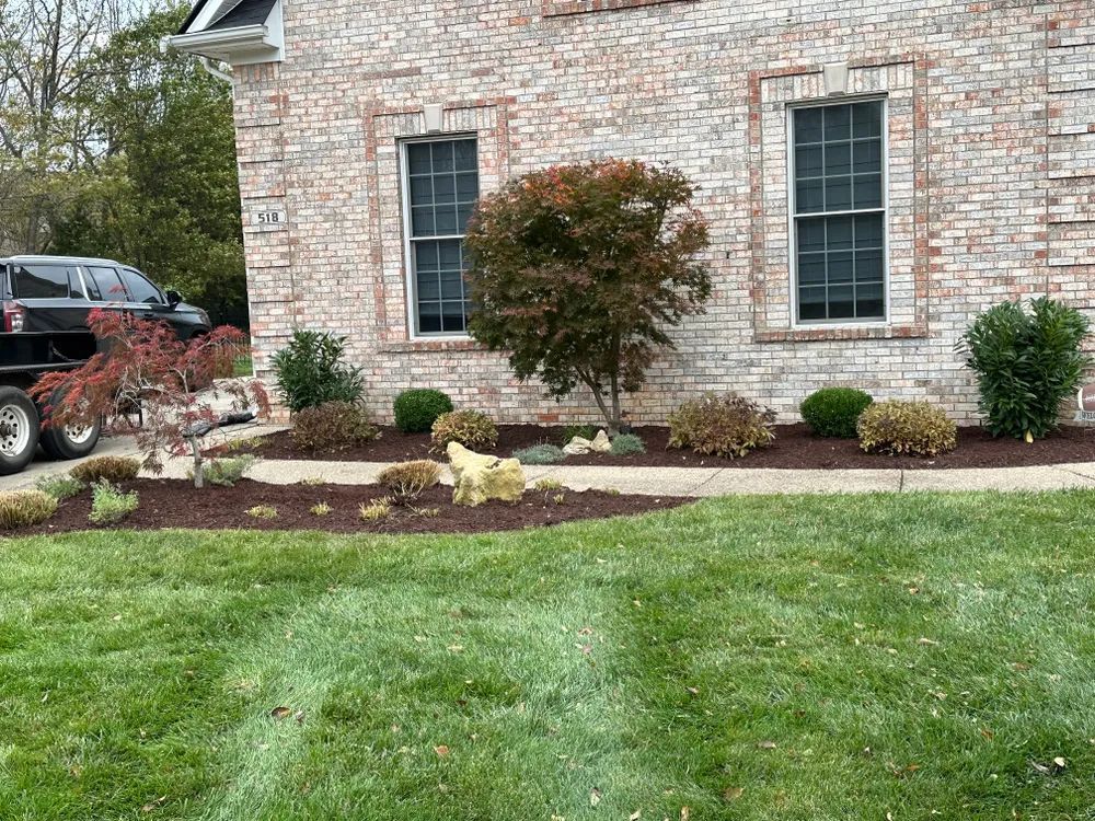 A brick house with a lush green lawn and a black suv parked in front of it.