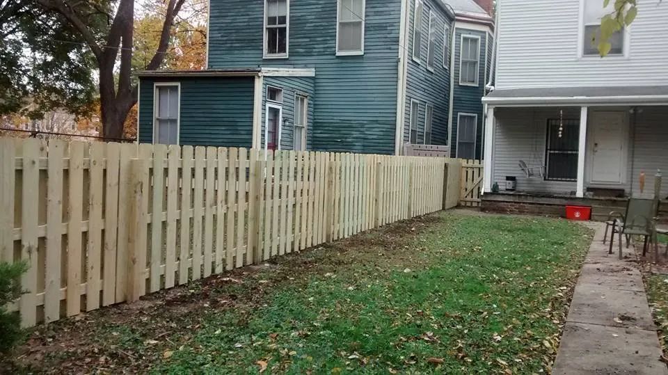 A wooden picket fence is in the backyard of a house.