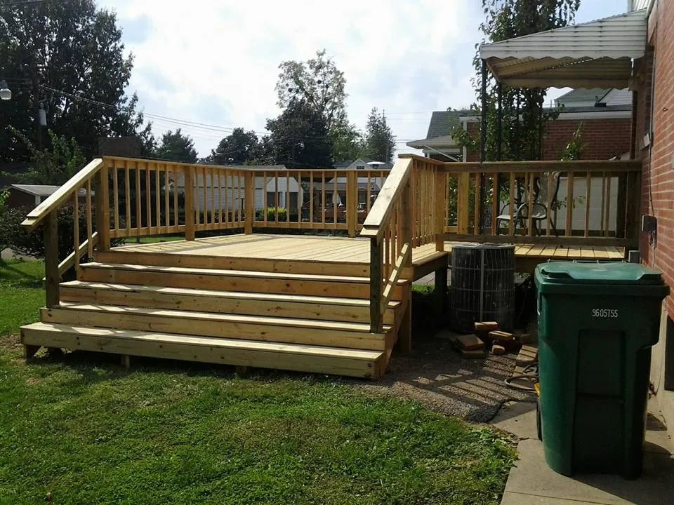 A wooden deck with stairs and a green trash can in front of it.