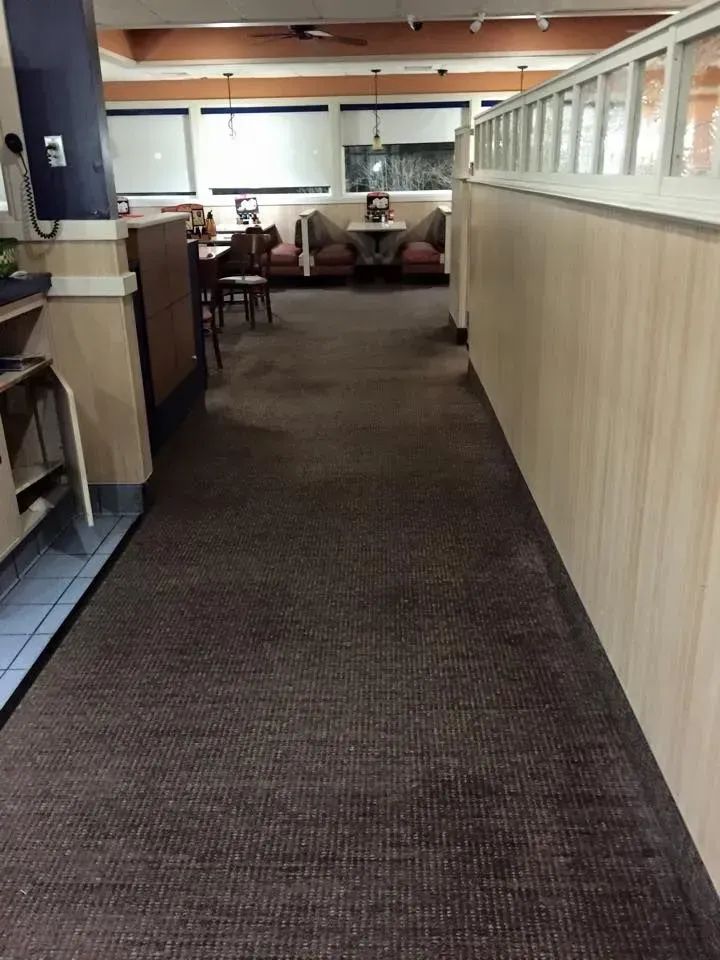 Restaurant aisle with brown carpet, booths, and wood paneling.