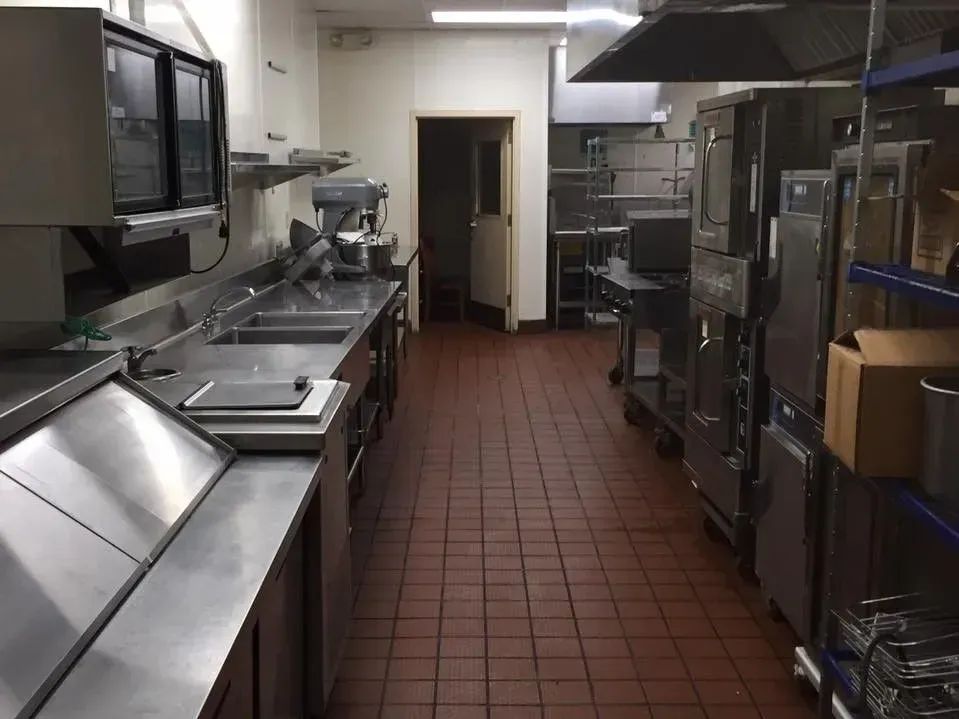 Commercial kitchen interior with stainless steel countertops, appliances, and red tile flooring.