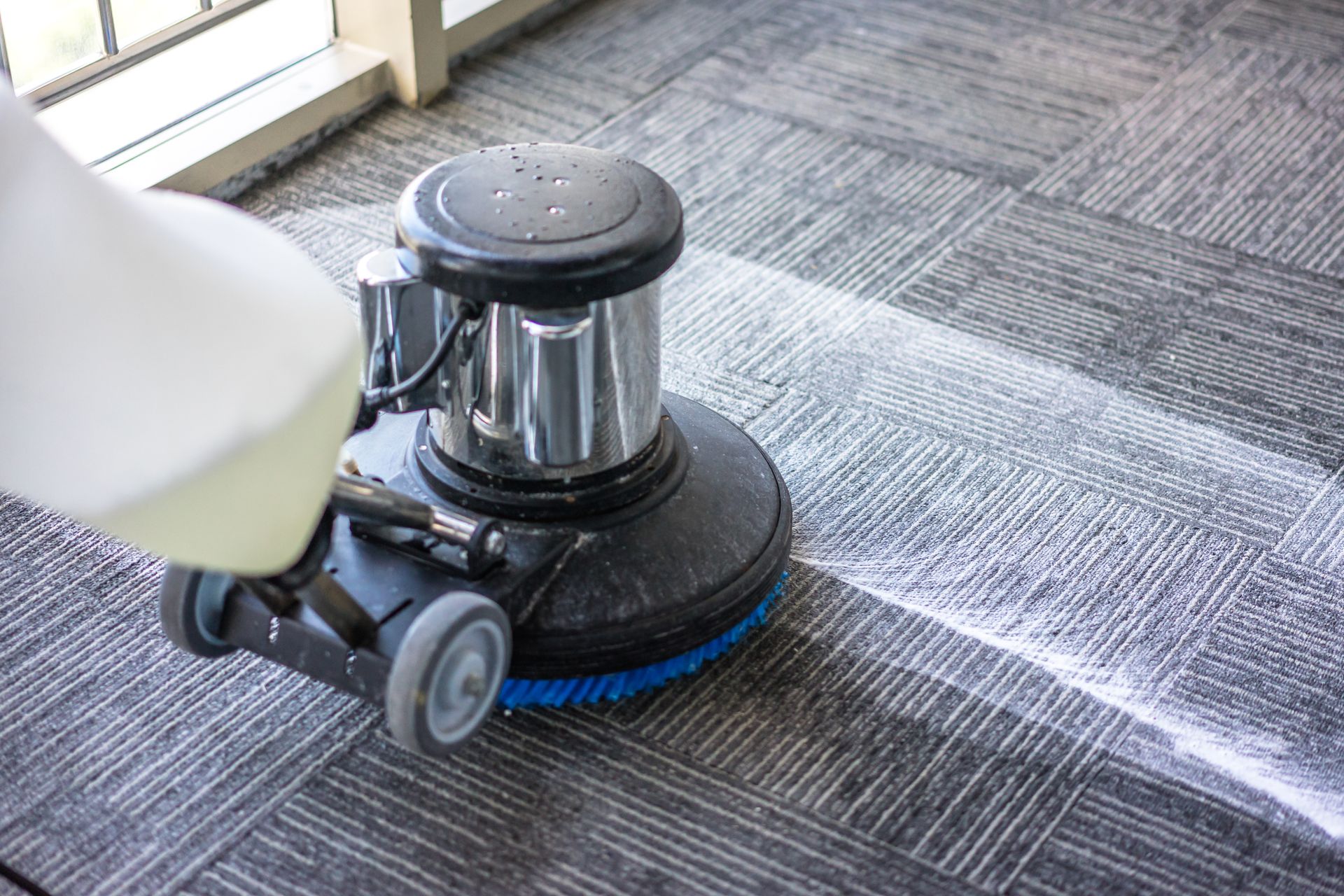 Carpet cleaning machine on a grey patterned carpet, dispensing cleaning solution.
