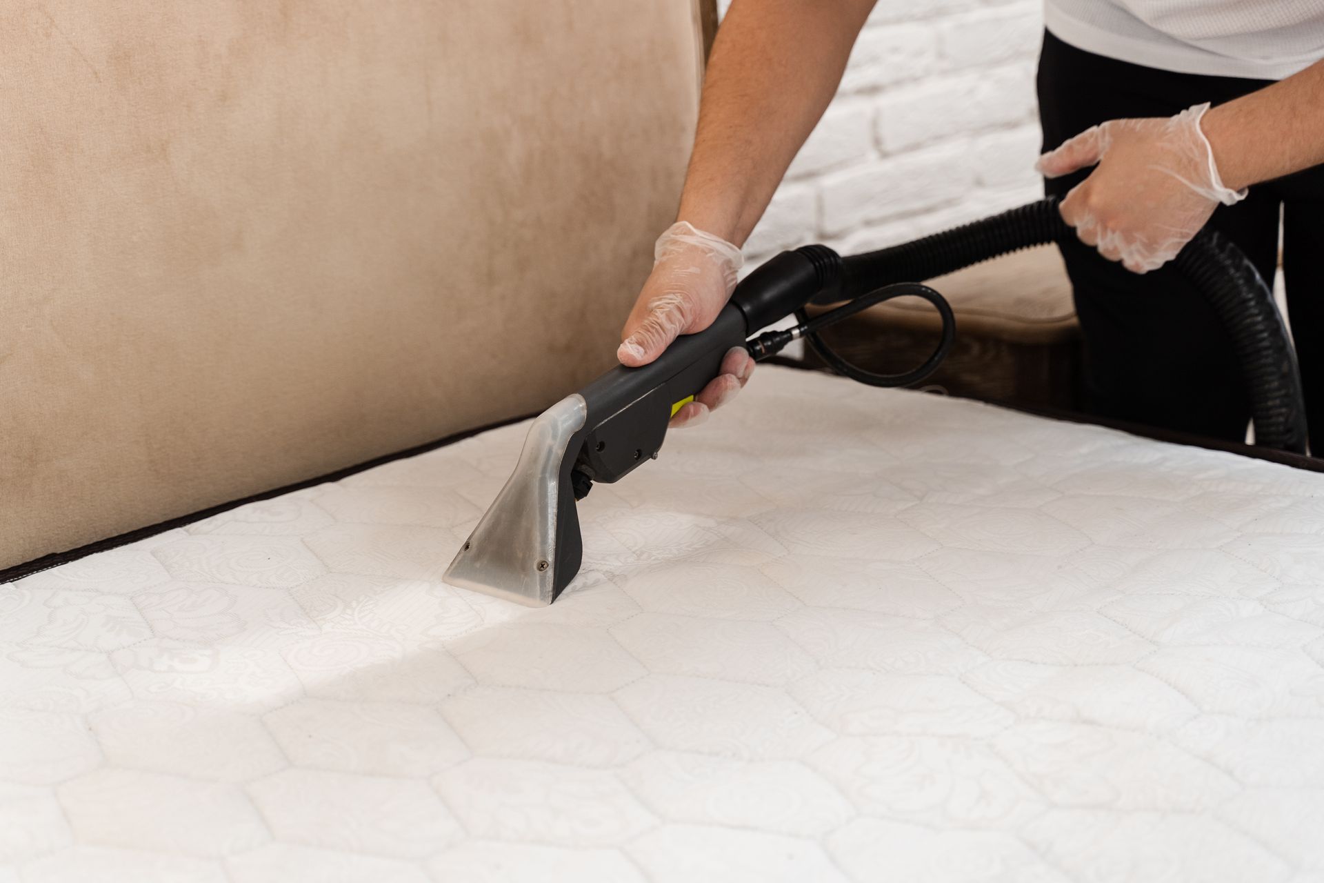 Person cleaning a white mattress with a vacuum, wearing gloves.