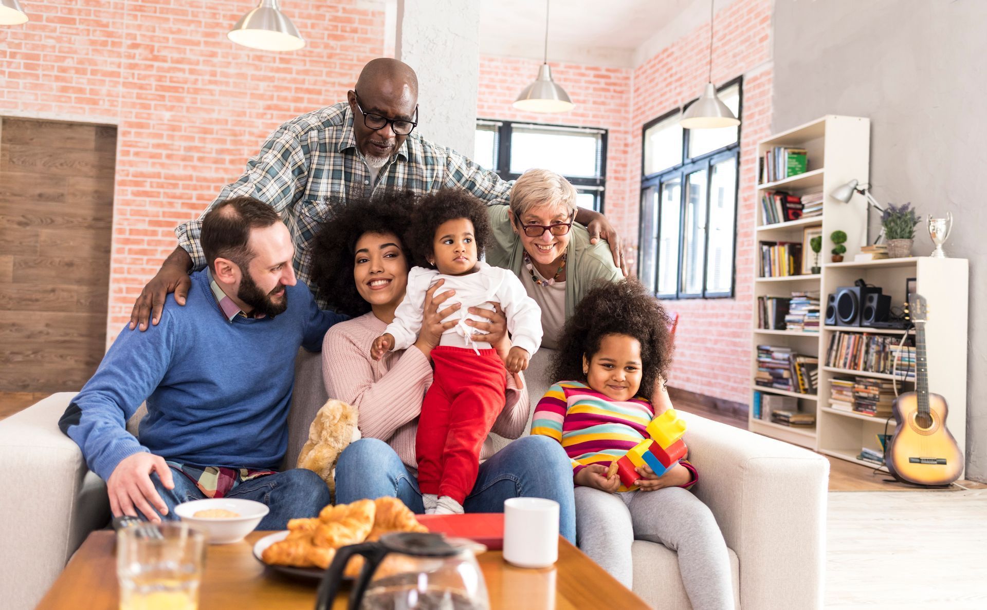 Family of seven seated together on a couch in a living room, smiling at camera.
