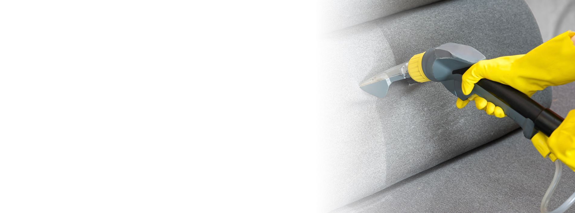 Person wearing yellow gloves cleans a gray couch with a handheld upholstery cleaner. Person wearing yellow gloves cleans a gray couch with a handheld upholstery cleaner.