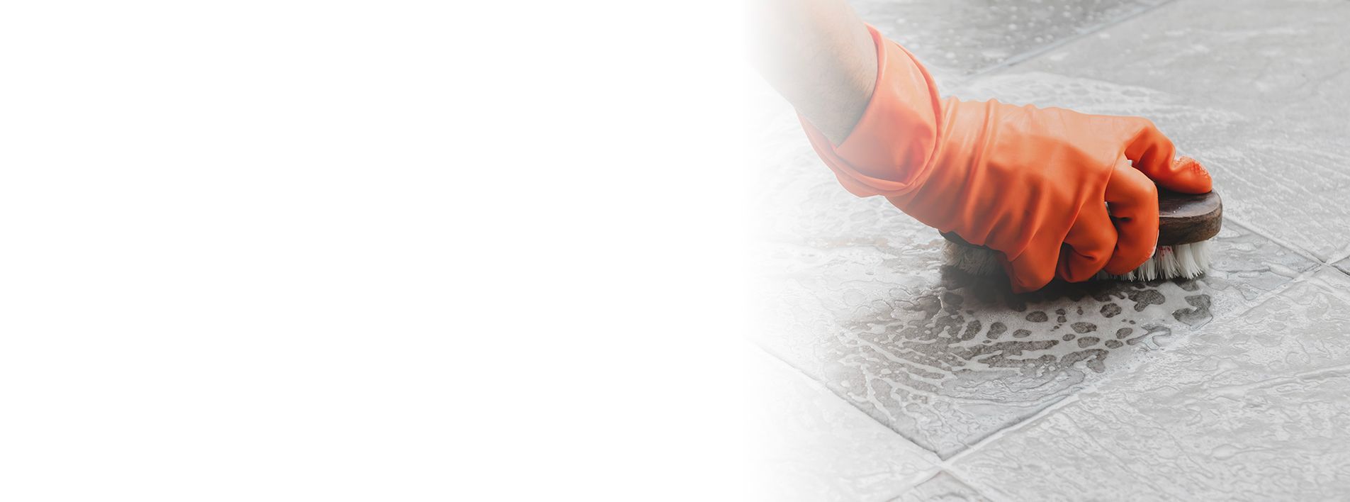 A person wearing an orange glove scrubs a tiled surface with a brush. A person wearing an orange glove scrubs a tiled surface with a brush.