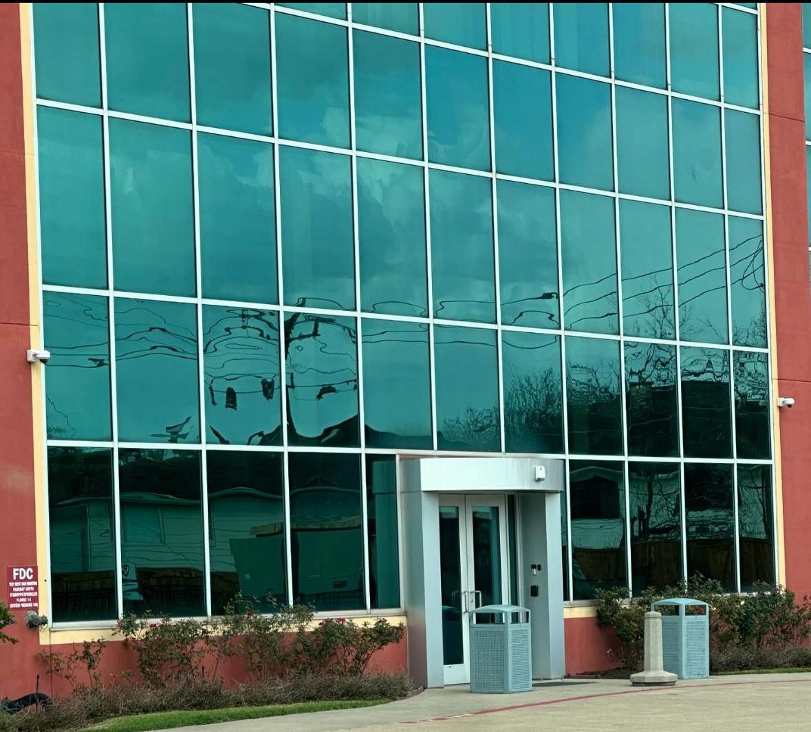 Building with teal tinted windows and a gray entrance; red exterior.