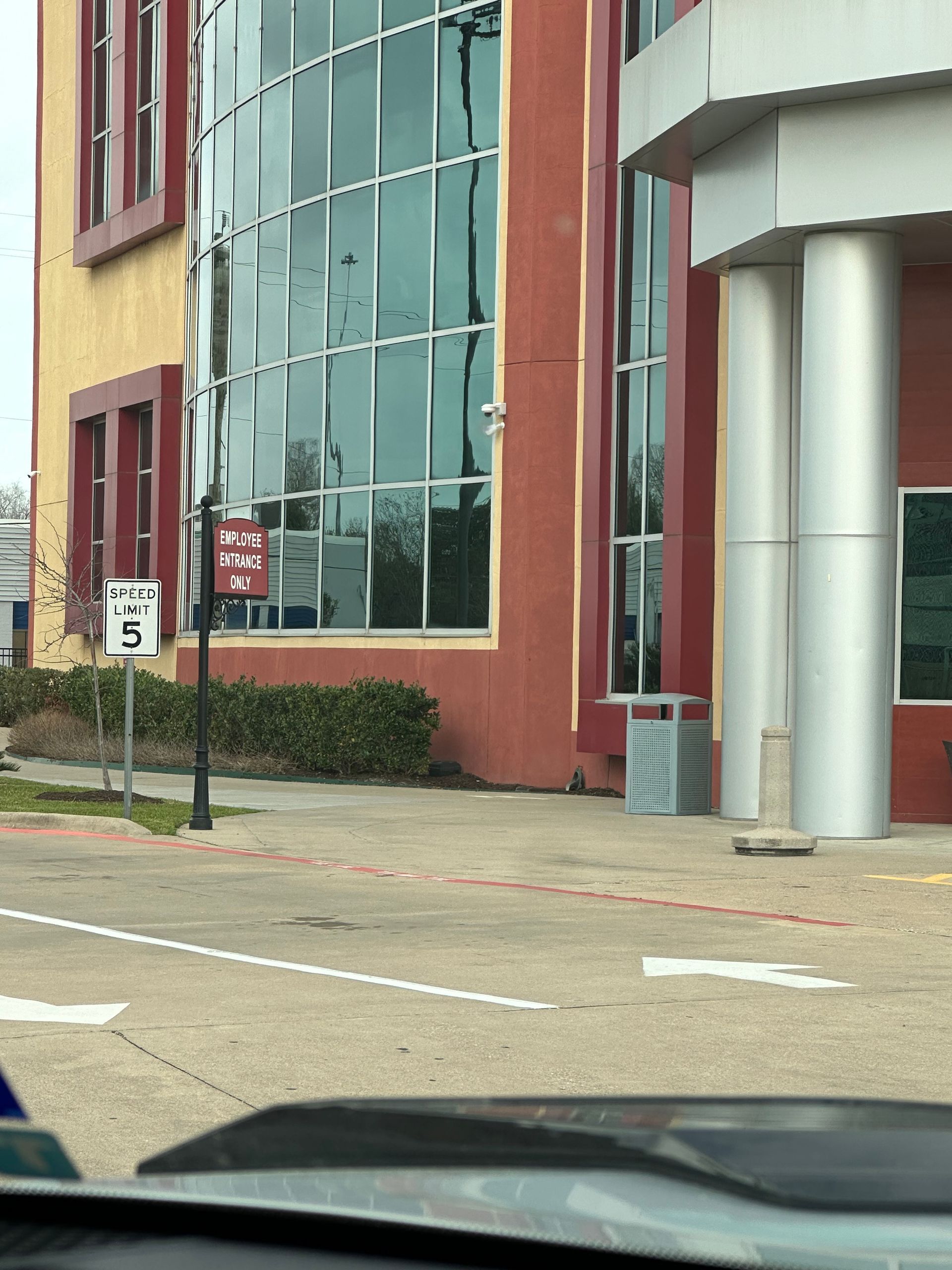 Exterior of a building with curved glass windows, red and tan facade, speed limit sign.