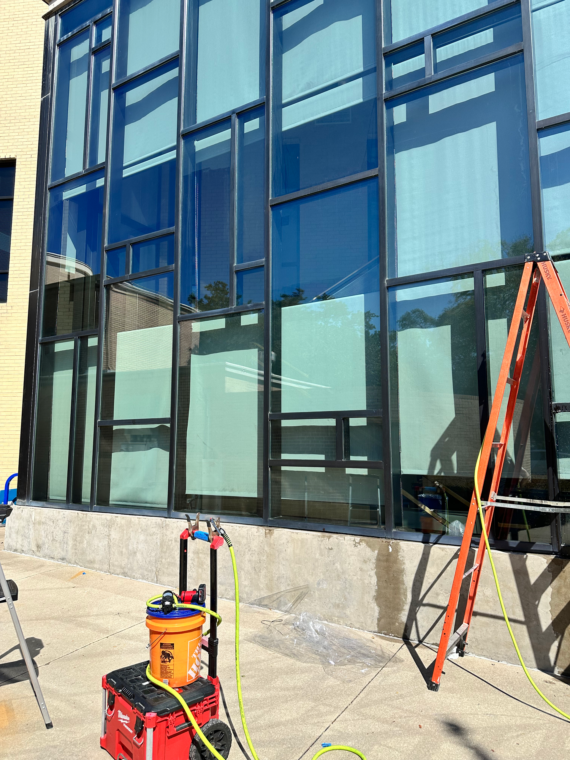 Building with large windows, a ladder, and cleaning equipment on a concrete patio.