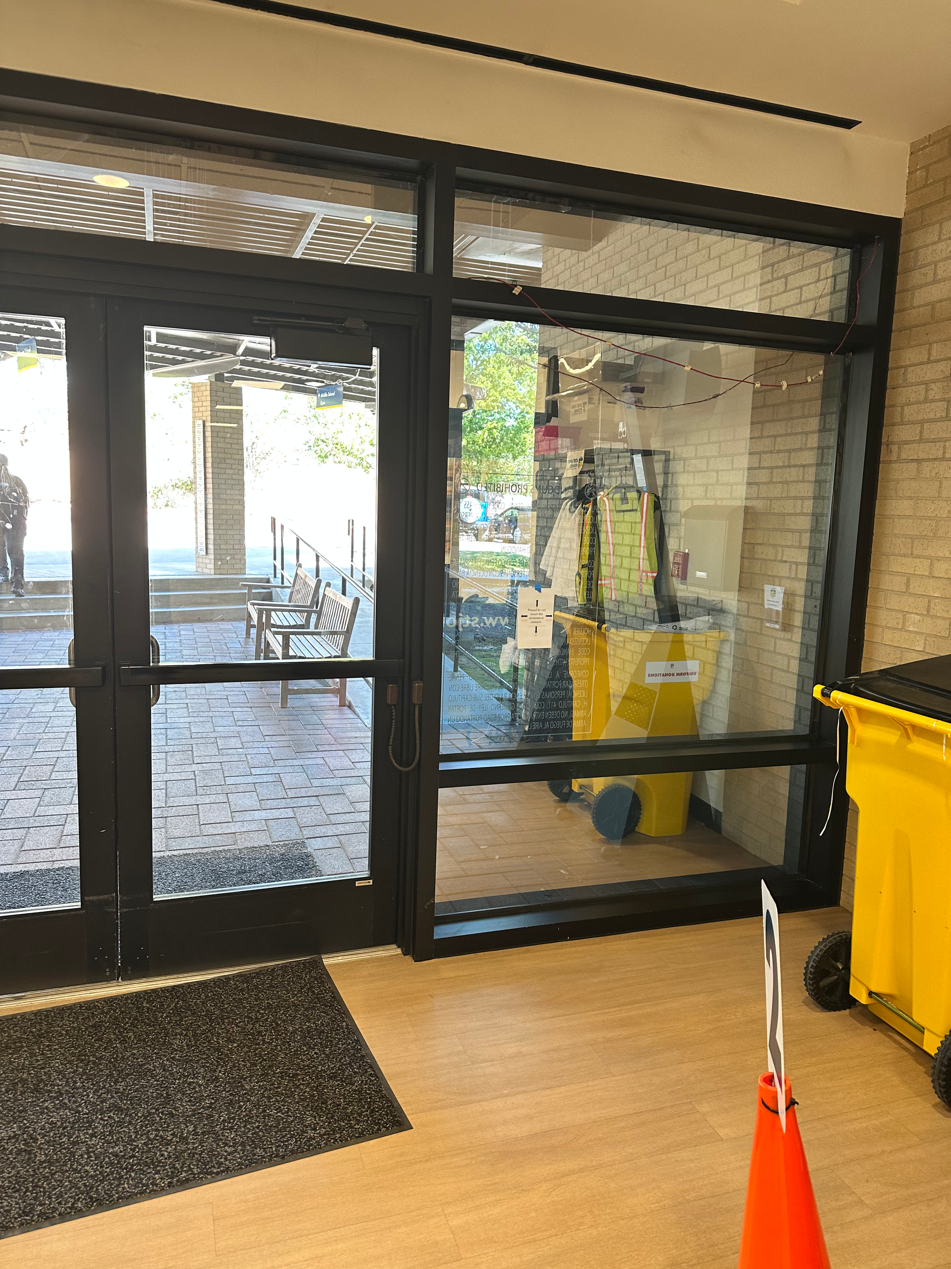 Entrance door with black frame and large window, with a yellow cleaning cart inside.