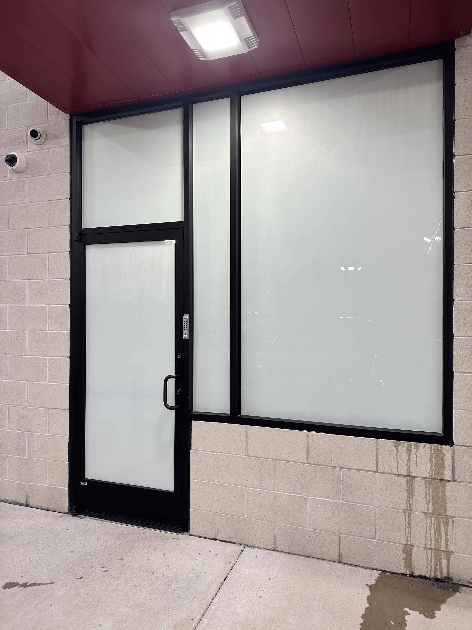 Black-framed commercial door and window with frosted glass on a brick building.