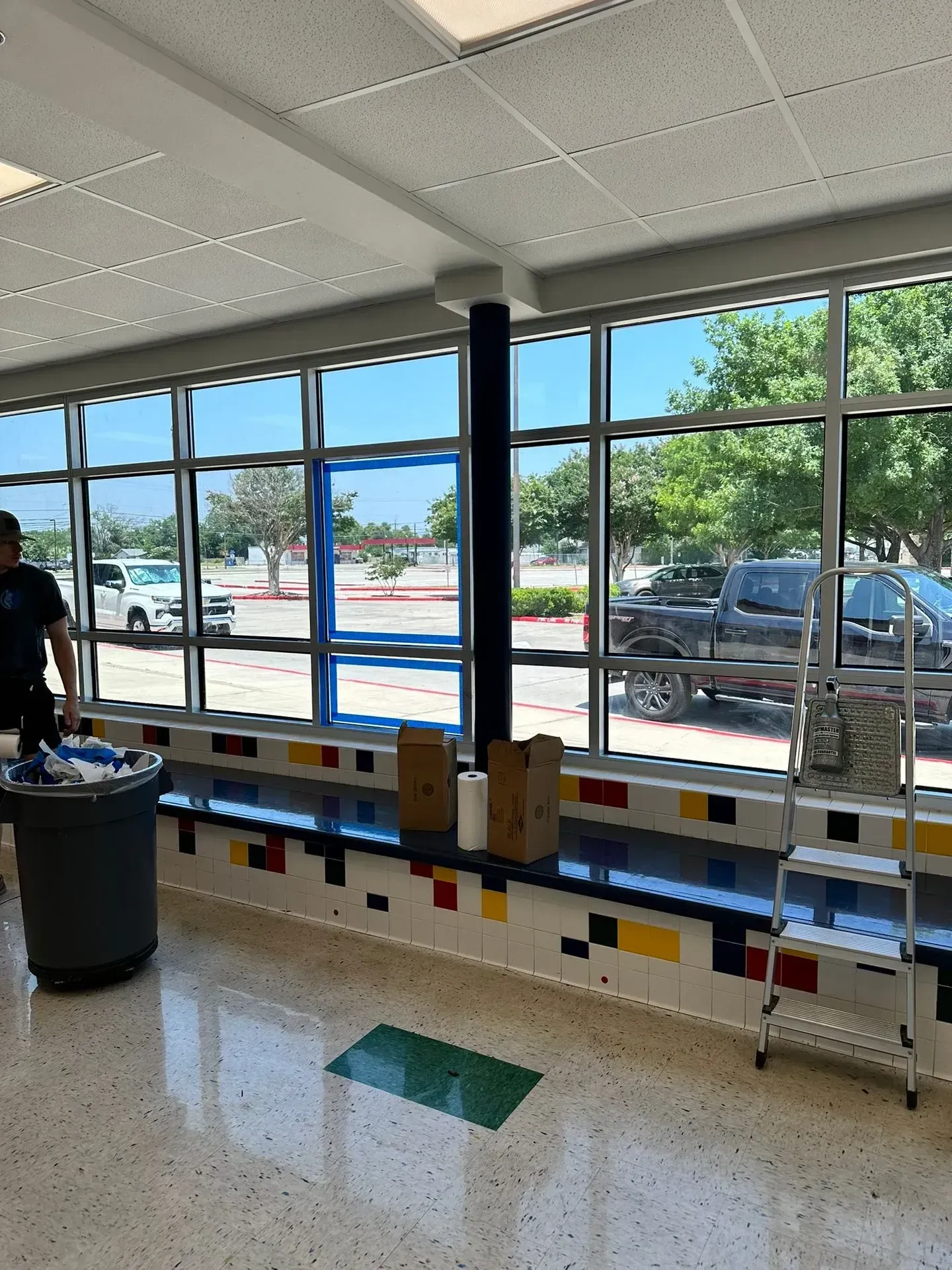 School hallway with large windows, a trash can, and a person.