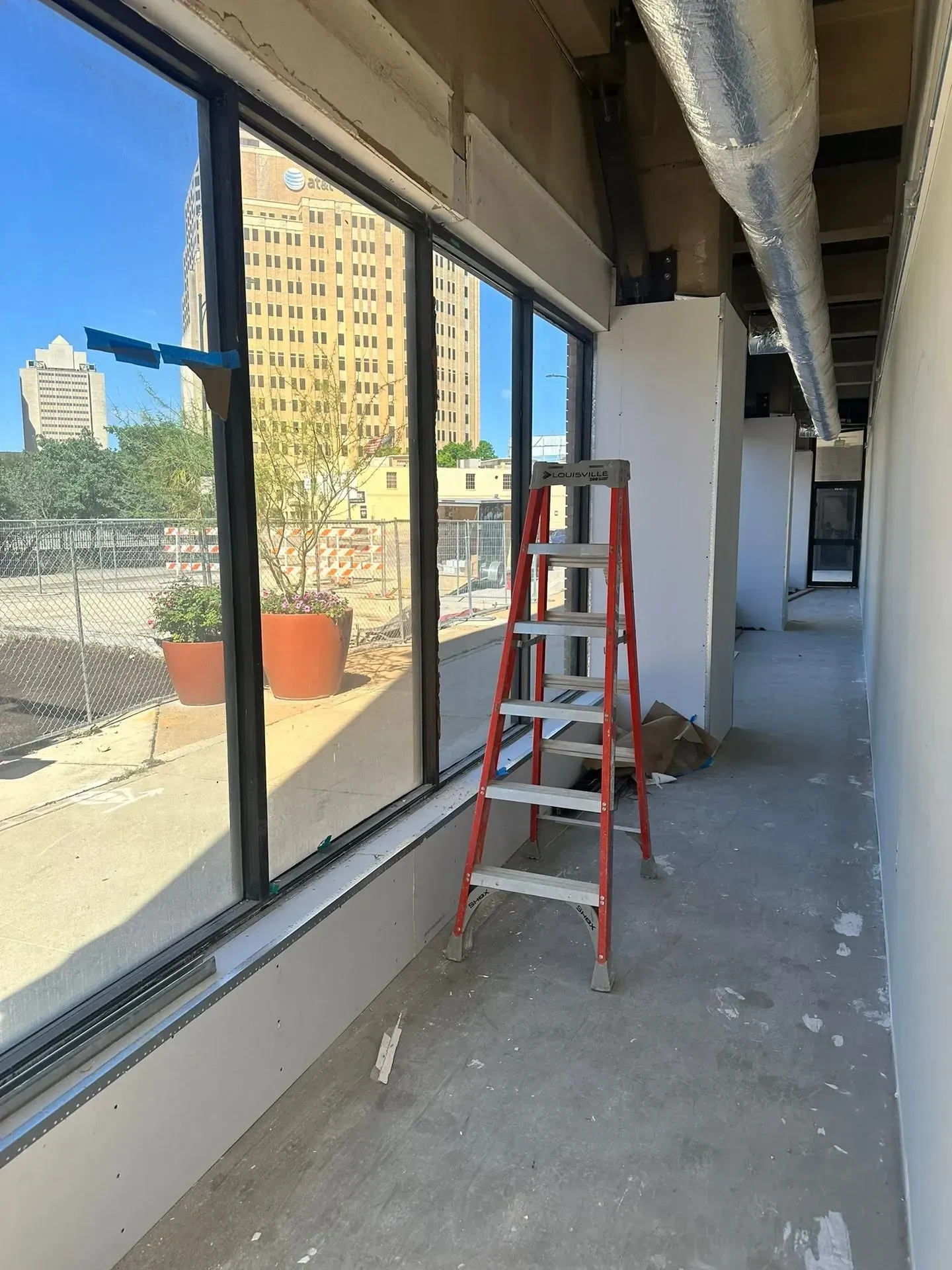 Interior view of construction site with a red ladder near a window overlooking a city.