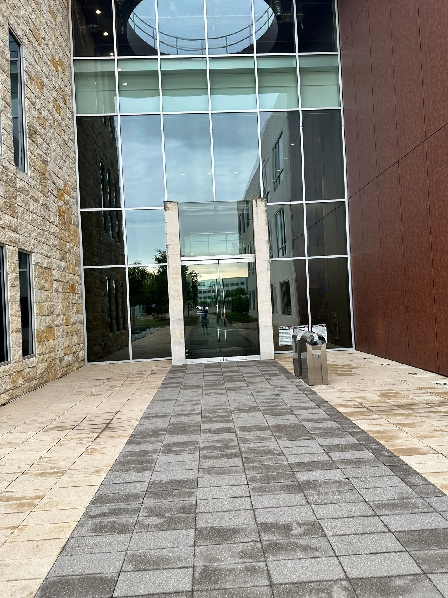 Entrance to a modern building, with glass doors, stone walkway, and a brick wall.