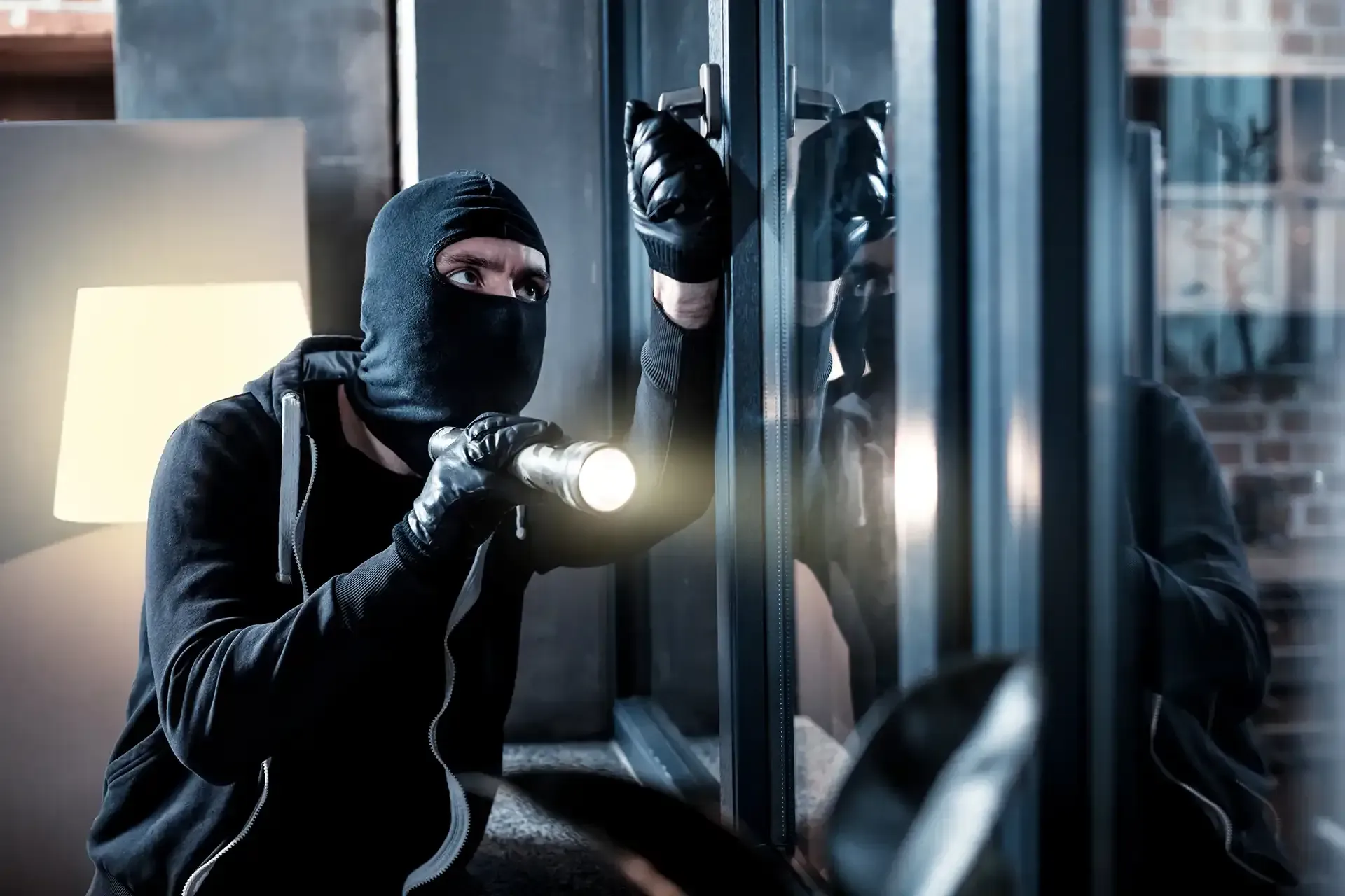 Person in a black balaclava, using a flashlight, attempting to open a door.