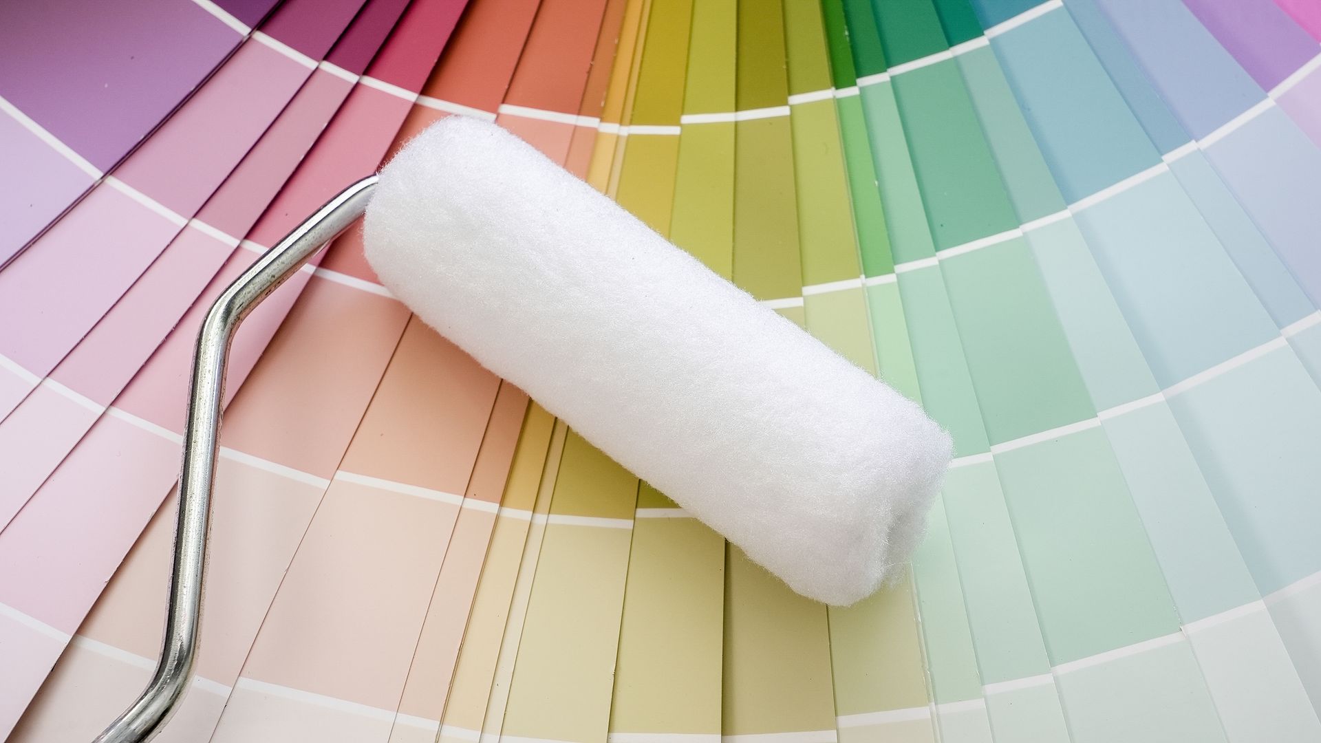 A white paint roller sits atop a colorful fan deck of paint swatches.