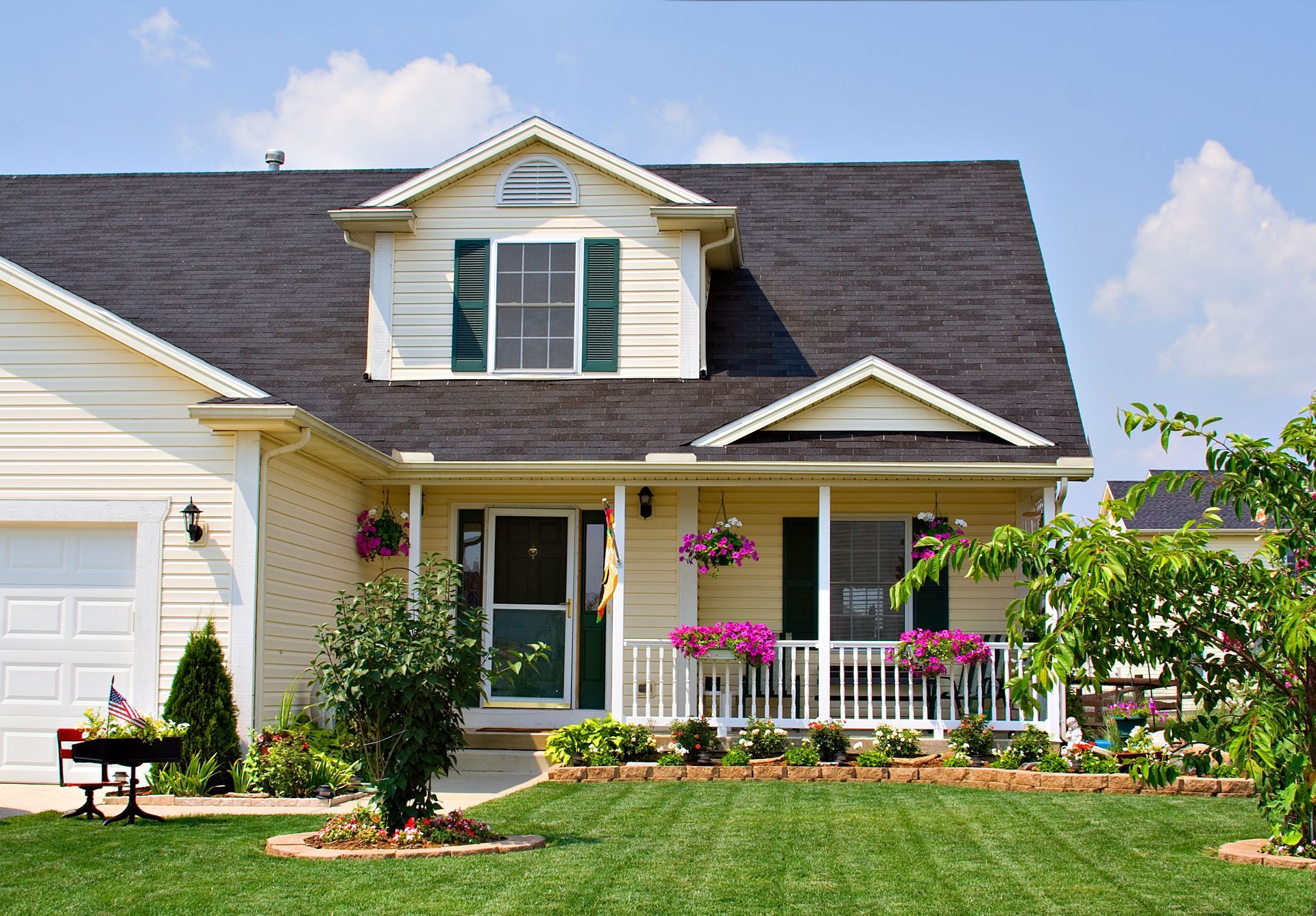 Beige house with gray roof, black shutters, and a ladder propped up.