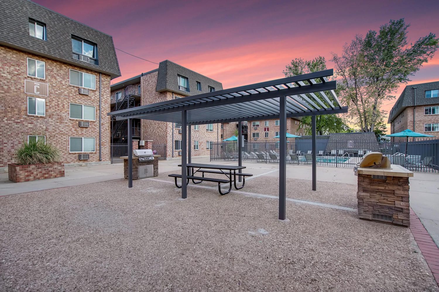 Outdoor community courtyard with a metal pergola, picnic table, and grill near poolside seating.