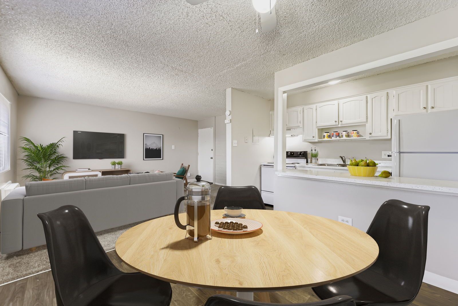 Open-concept living area with round wooden dining table, gray sofa, and white kitchen cabinets.