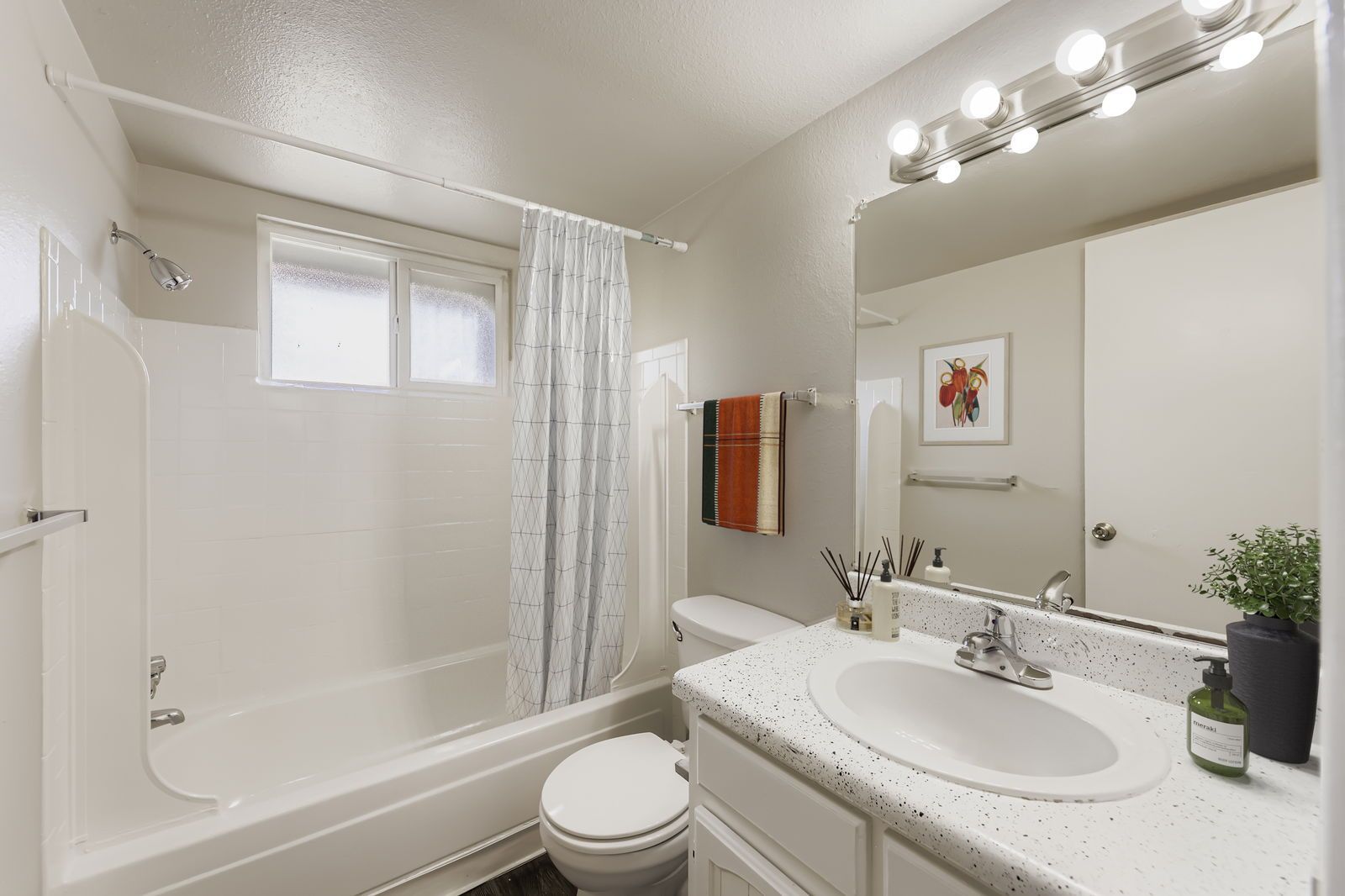 Bathroom in a residential apartment with tub/shower, sink, mirror, and window.
