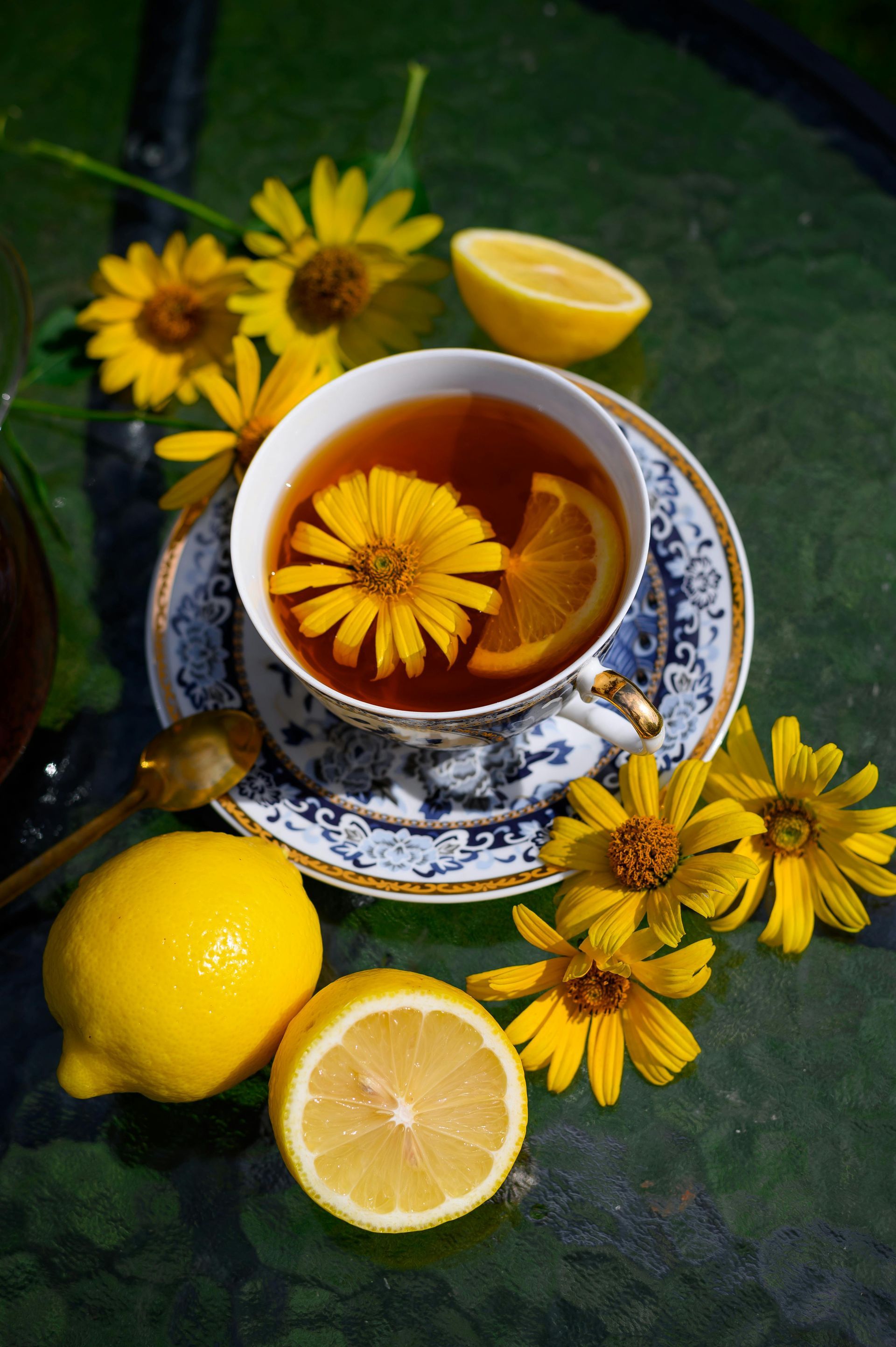 Cup of tea with lemon and yellow flowers, on a glass surface.