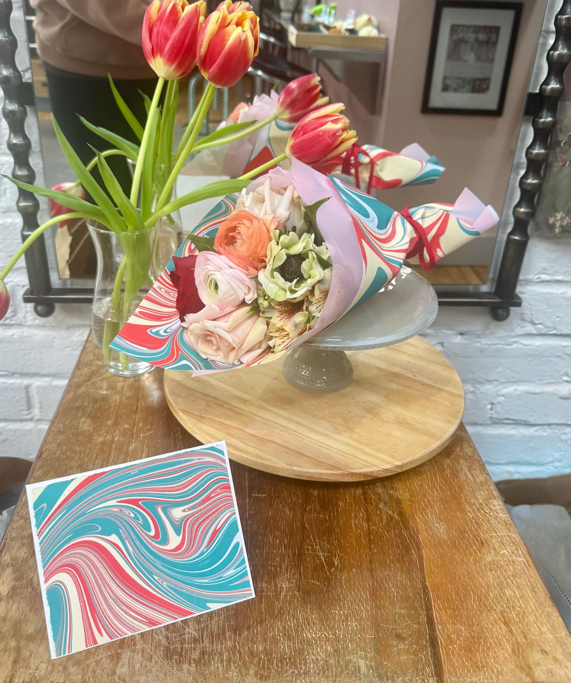 Bouquet of flowers, tulips in vase, and marbled stationery on a wooden table.