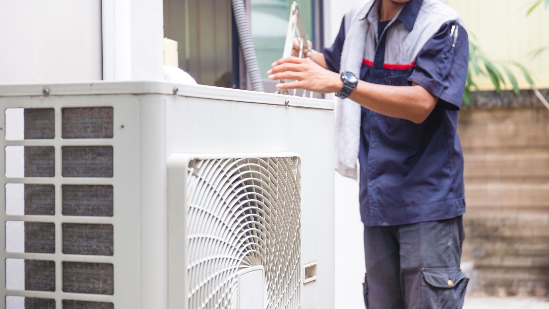 A man is working on an air conditioner outside of a building.