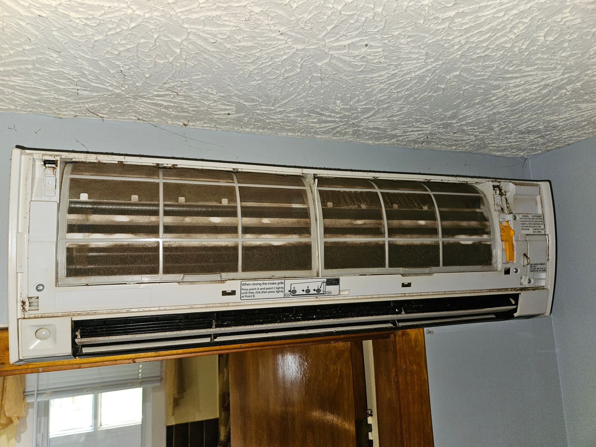 A dirty air conditioner is hanging on a wall in a room