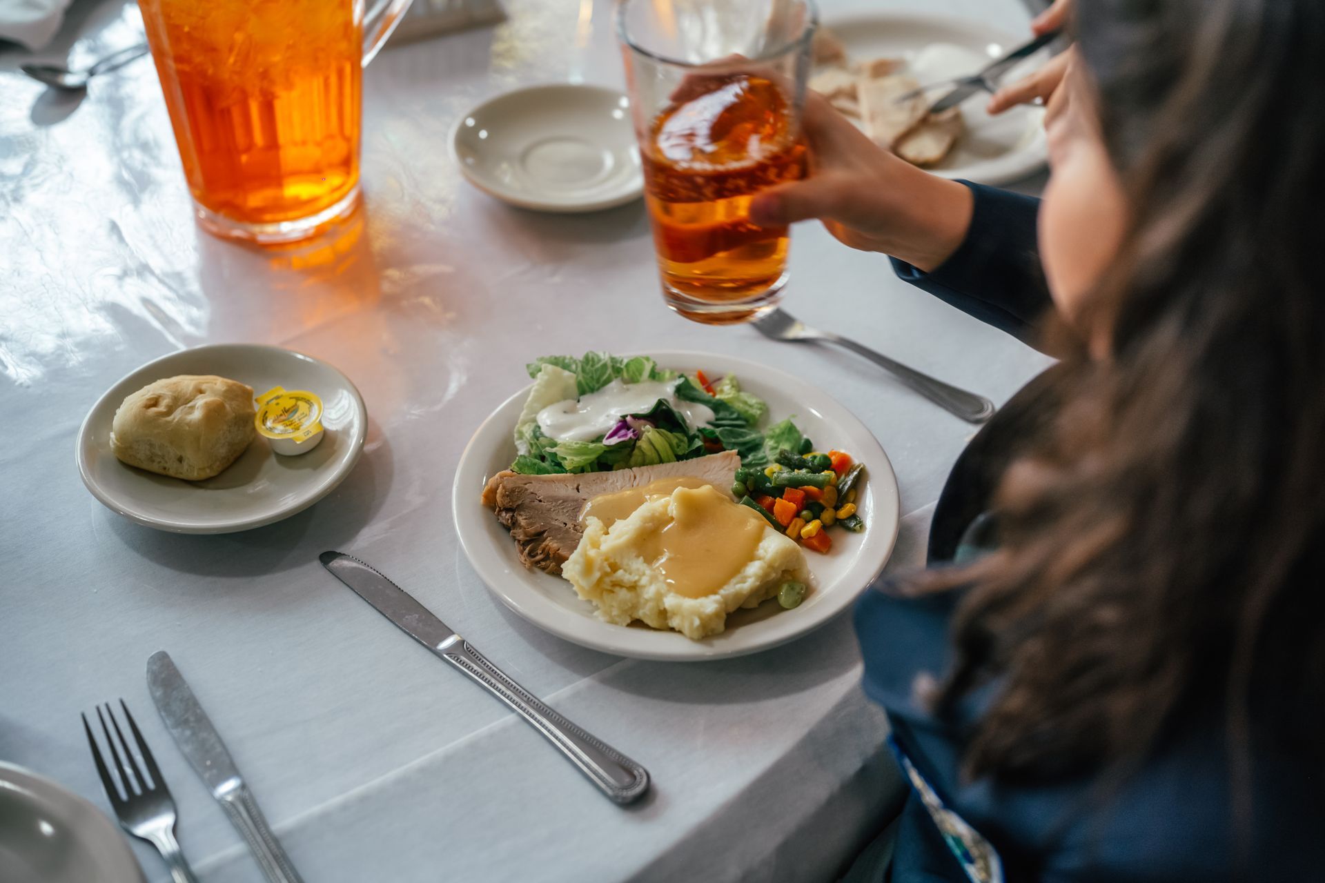 Person at a table with a plate of food, drink, and biscuit.