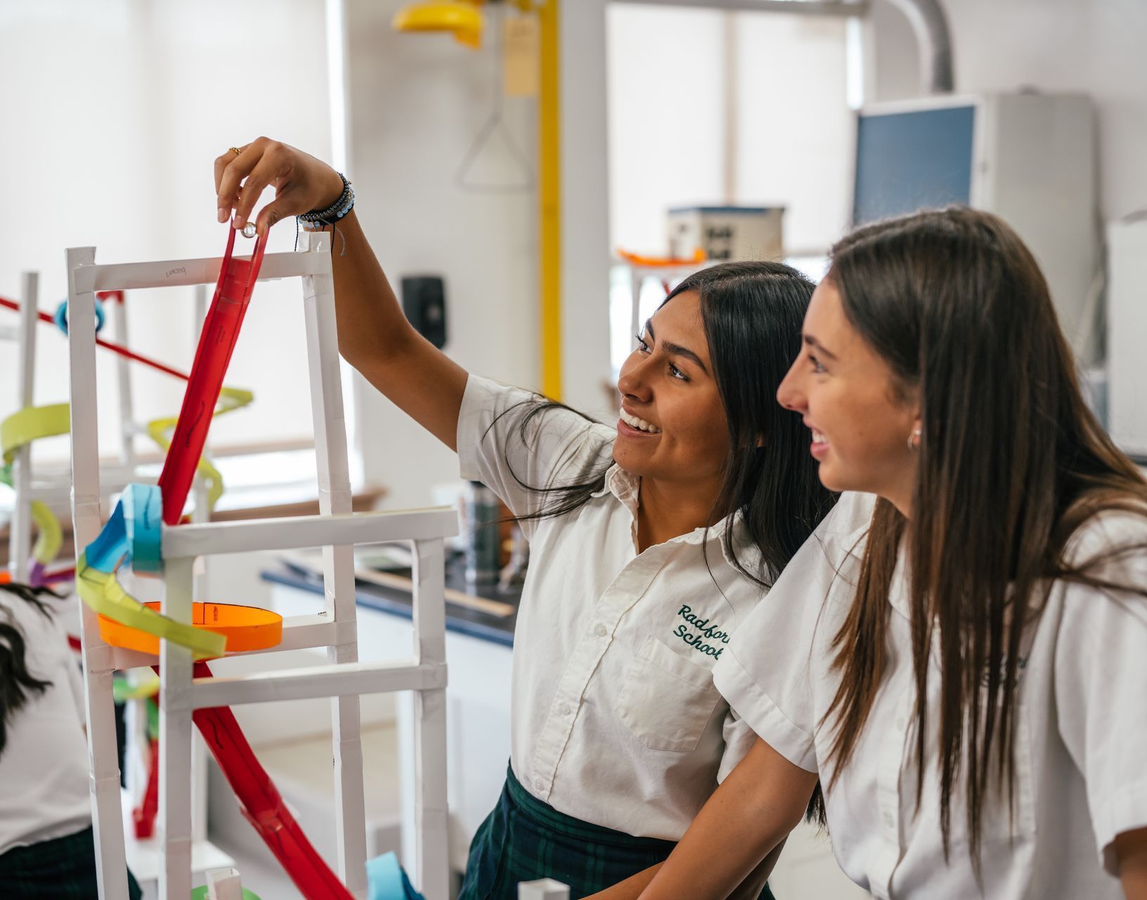 Two young women in lab coats building a roller coaster. They are smiling in a lab setting.