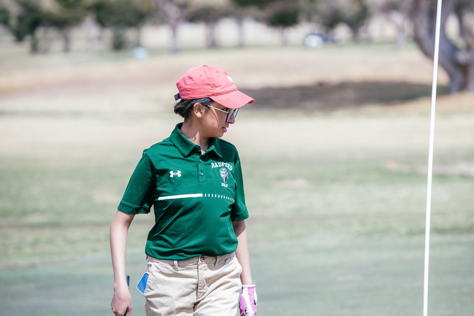 Person in green shirt and red cap on a golf course, looking toward the flag.