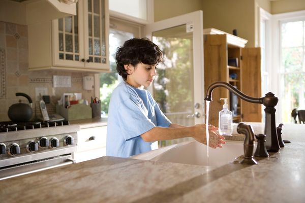 A young child is washing his hands at the kitchen sink. All water in a household with a septic system will eventually drain through the septic tank,
