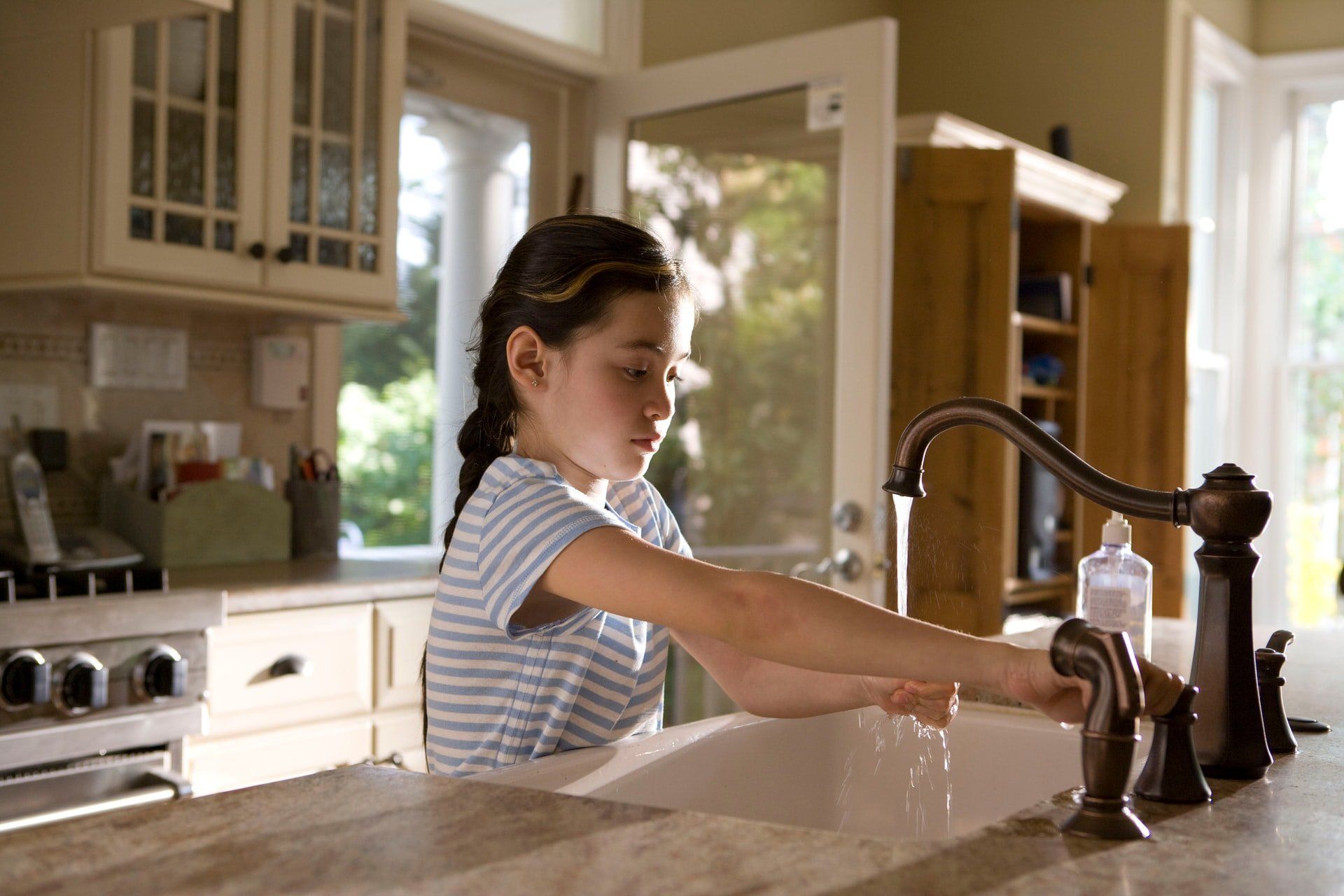 A young girl is washing his hands at the kitchen sink. All water in a household with a septic system will eventually drain through the septic system.