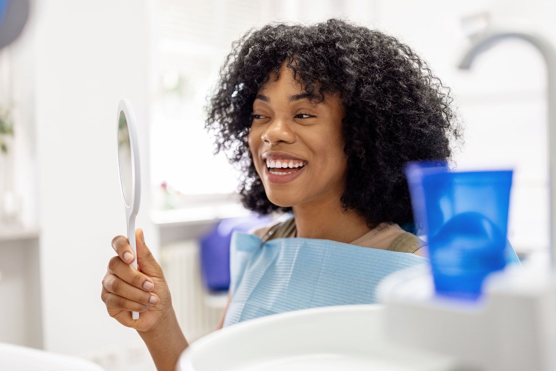 Afro-American woman checking her teeth at a dentist office after a procedure.