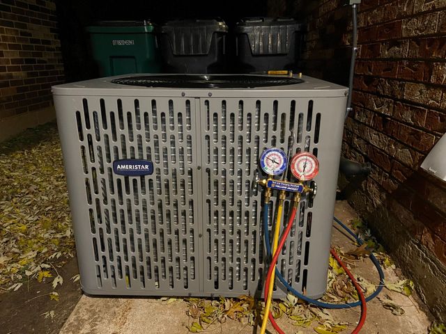 A gray air conditioner is sitting on the ground next to a brick wall.