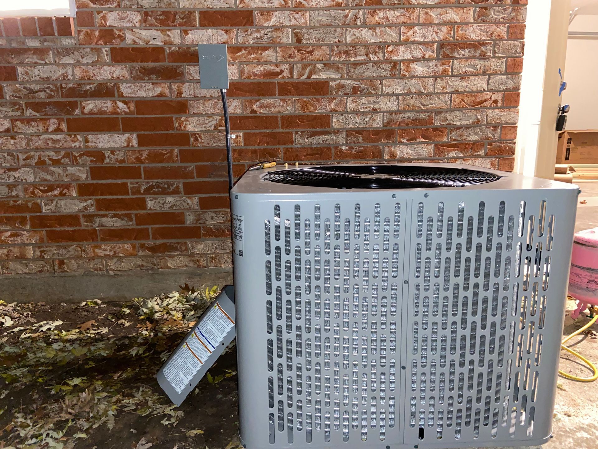 An air conditioner is sitting in front of a brick wall.