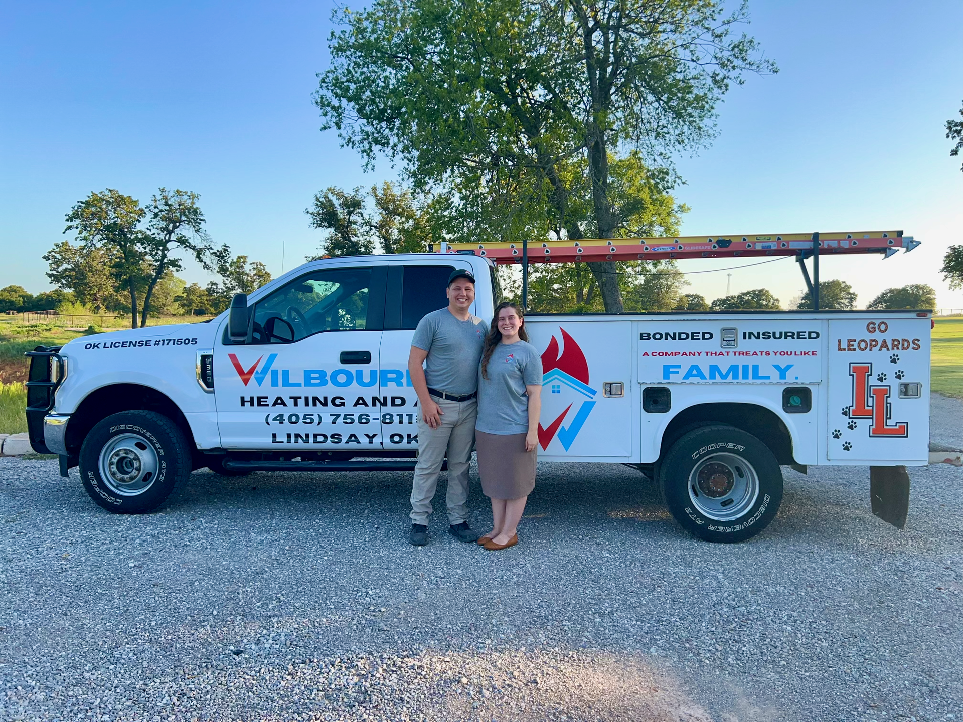 A man and a woman are standing in front of a heating and cooling truck.
