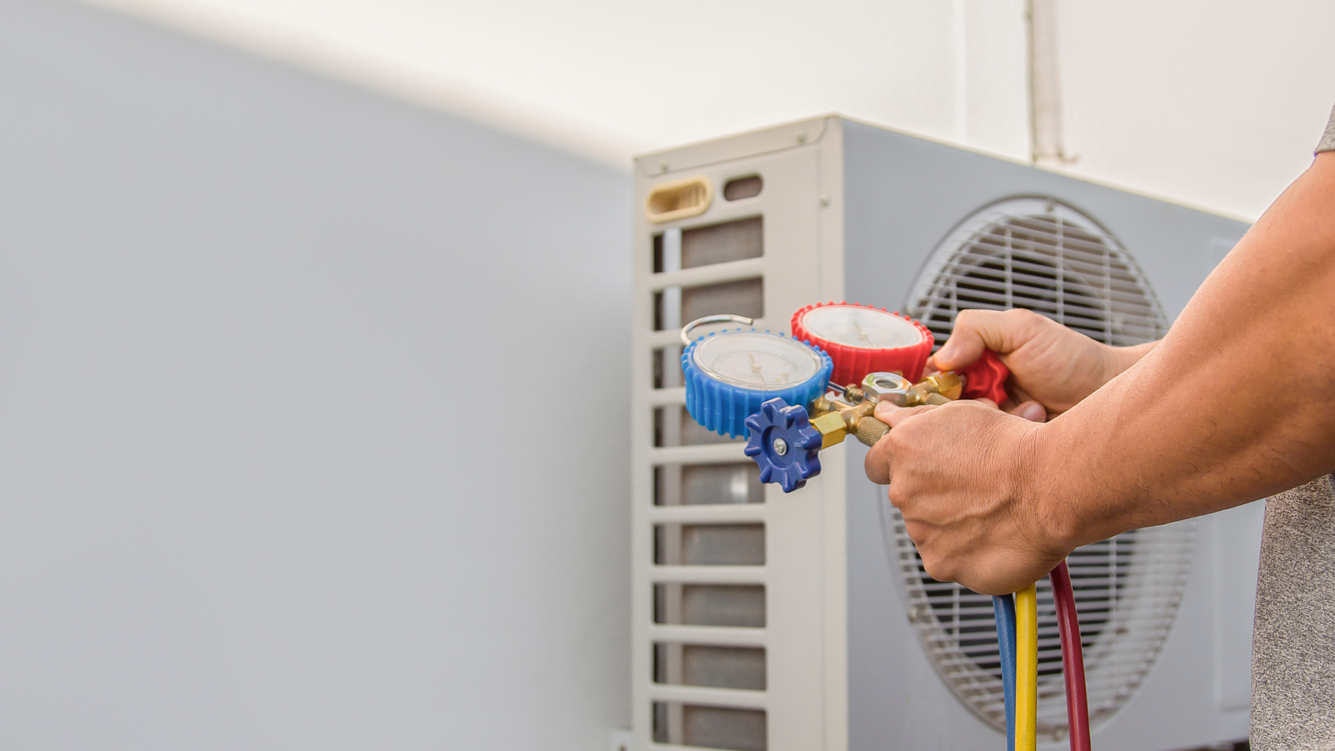 A man is working on an air conditioner with a gauge.