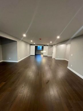 Empty modern basement with dark wood floors, gray walls, recessed lights, and a doorway to daylight.