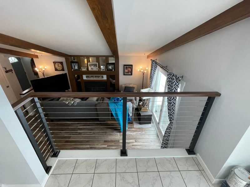 Loft staircase view into a living room with wood floors, white walls, and a railing in the foreground