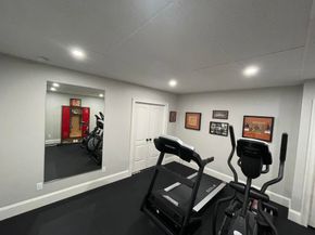 Small home gym with treadmill, elliptical, wall mirror, and framed art on gray walls.