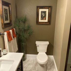 Bathroom with white toilet, sink, mirror, towel rack, and potted plant on beige walls.