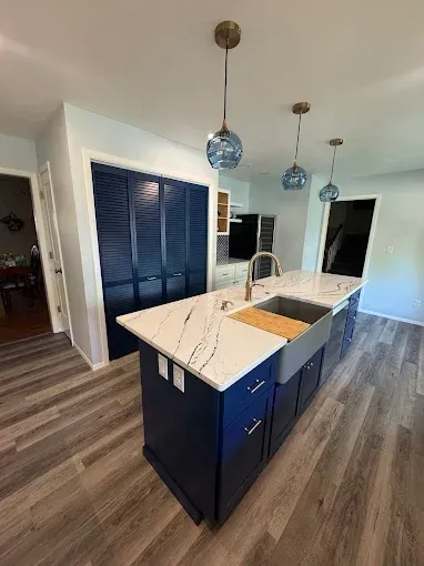 Modern kitchen with navy island, white countertops, pendant lights, and wood-look flooring