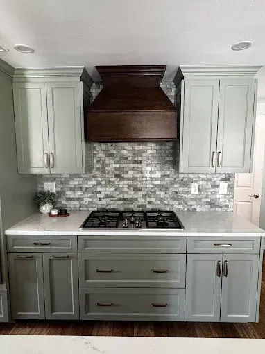 Modern kitchen with gray cabinets, white countertops, mosaic backsplash, and dark wood range hood