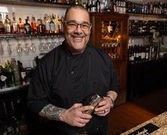 A man is standing in front of a bar holding a shaker.