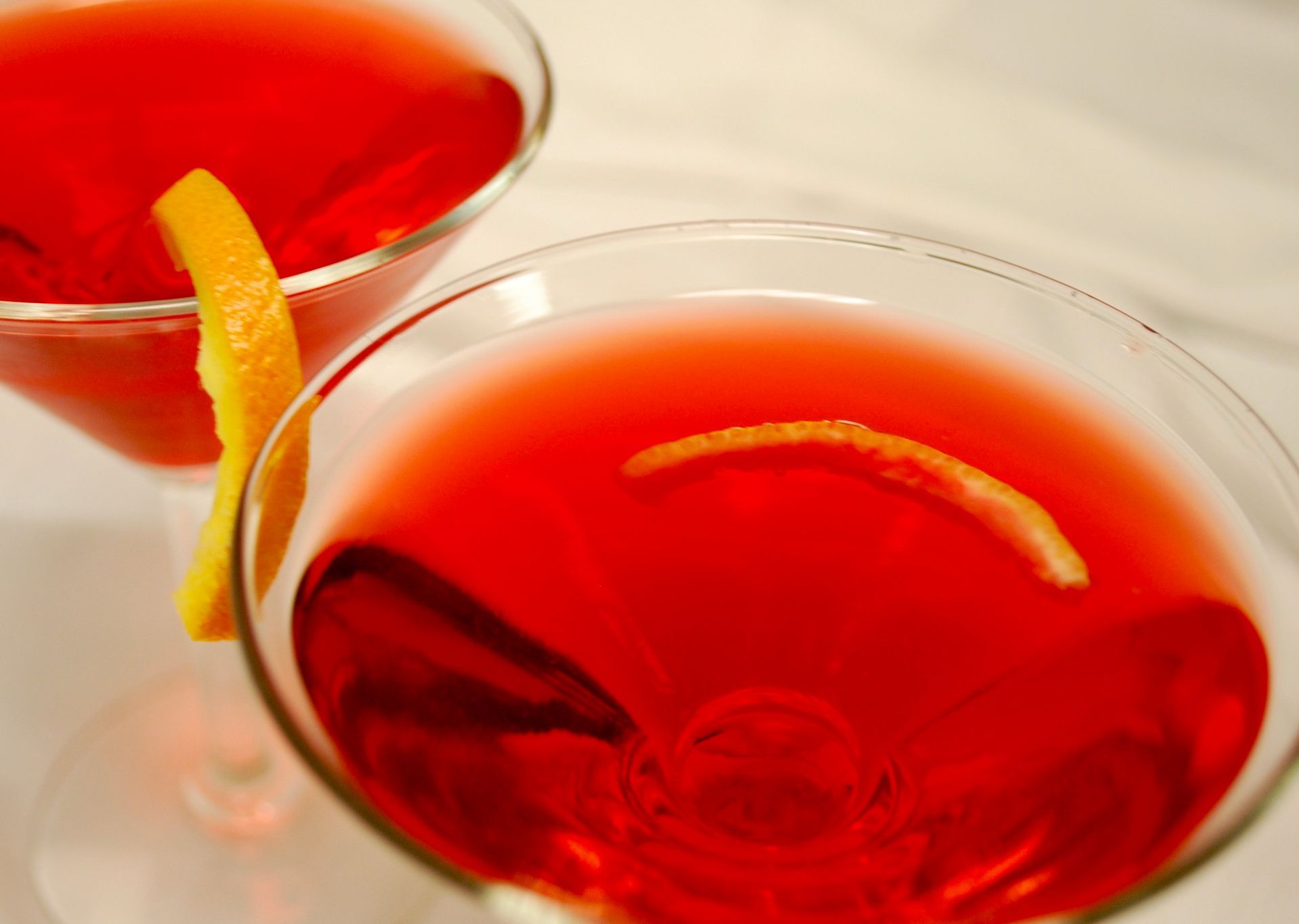 Two martini glasses filled with red liquid and an orange peel